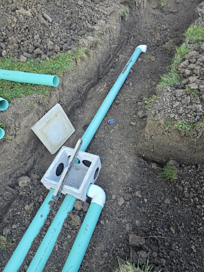 Freshly installed distribution box with green PVC piping in an open trench